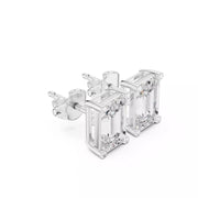 A pair of silver stud earrings featuring rectangular emerald-cut clear gemstones in a prong setting, shown on a plain white background.
