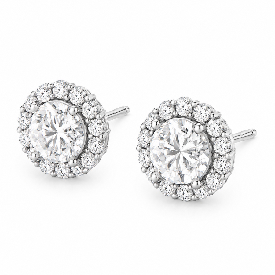 A pair of round halo stud earrings featuring a large clear center stone surrounded by a halo of smaller clear stones, set in 14k gold  on a plain white background.